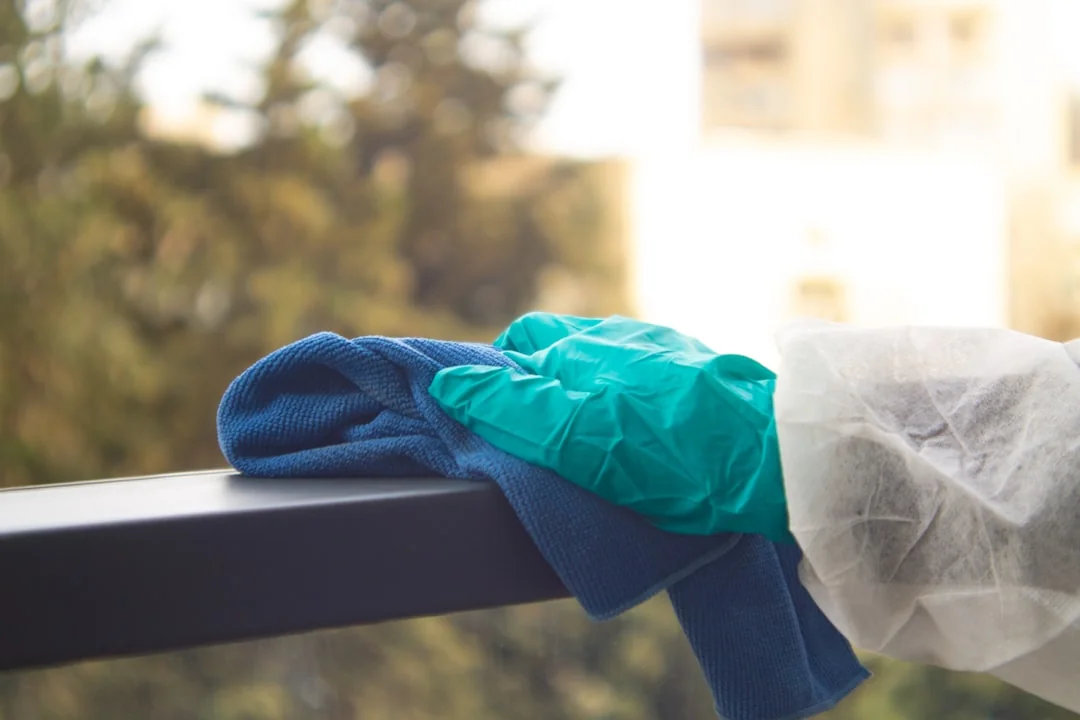 A man cleaning a glass barrier outdoors with a squeegee, surrounded by greenery.